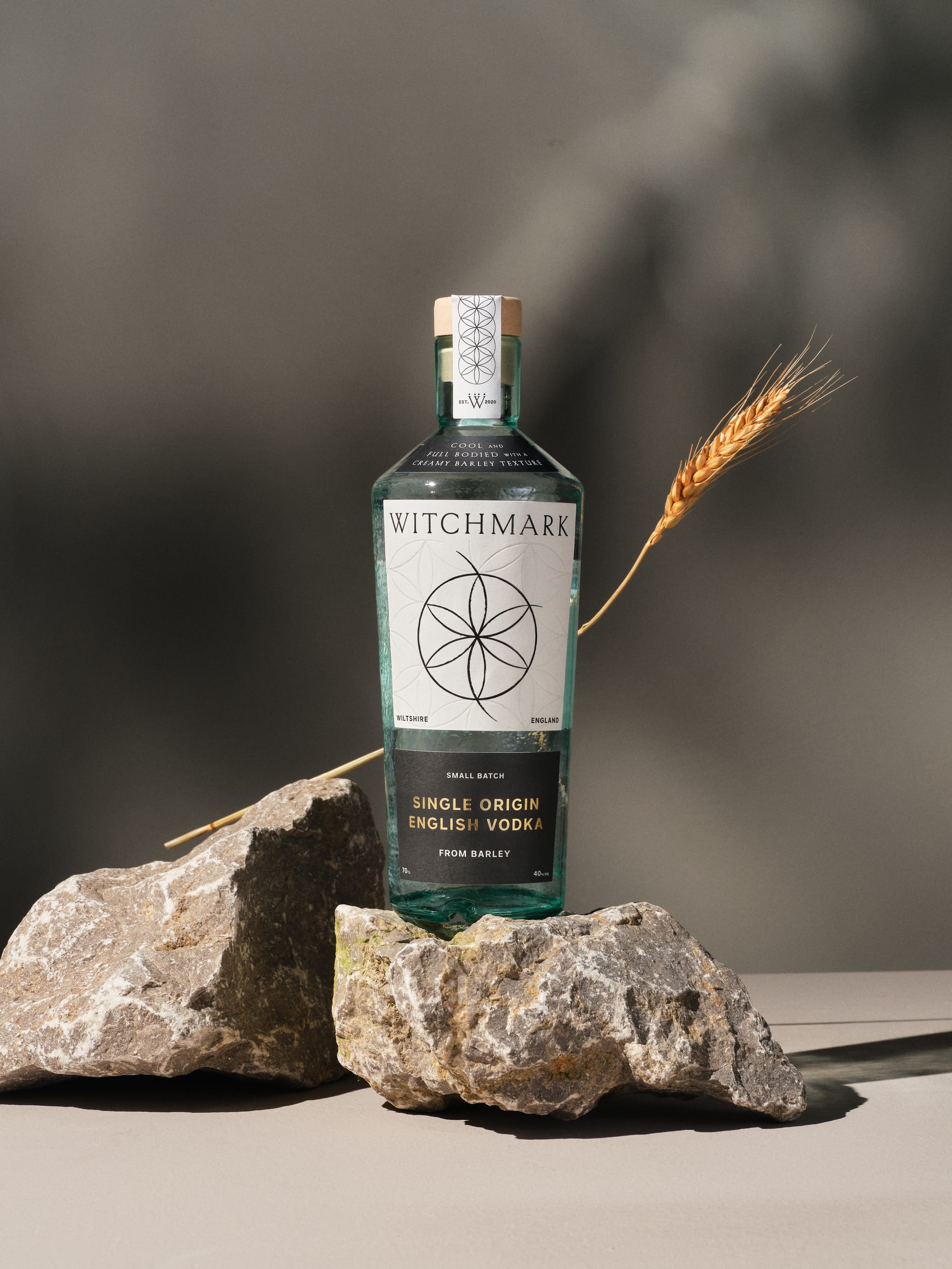 Marketing photo of a bottle of vodka balanced on two pieces of irregularly shaped stone. An ear of barley has been placed behind the bottle.